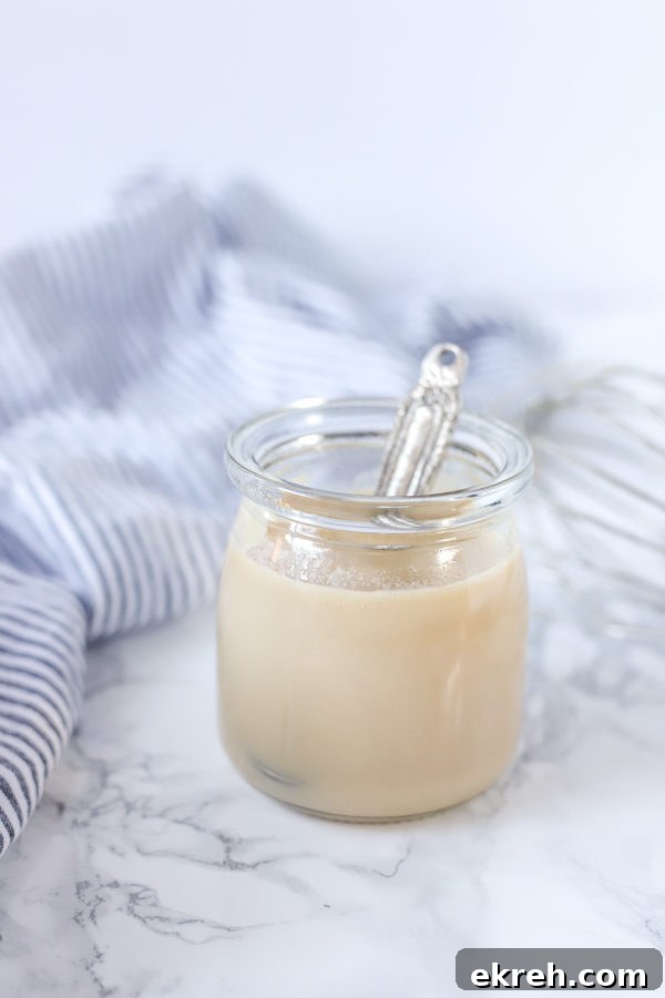 Homemade Sweetened Condensed Milk Recipe 3 glass jar of homemade sweetened condensed milk with a antique silver spoon coming out. a blue and white stripped towel is in the background