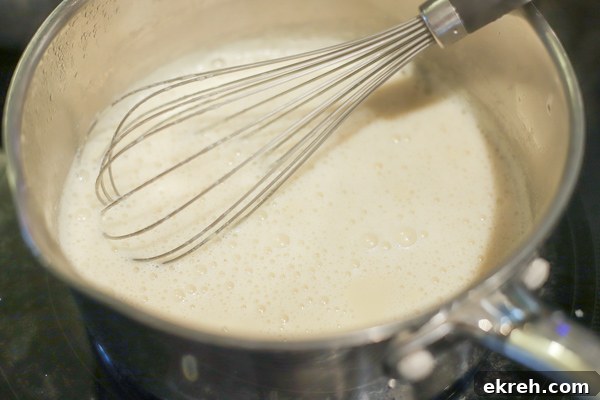 Homemade Sweetened Condensed Milk Recipe 5 simmering milk, cream, and maple syrup in a saucepan with a whisk