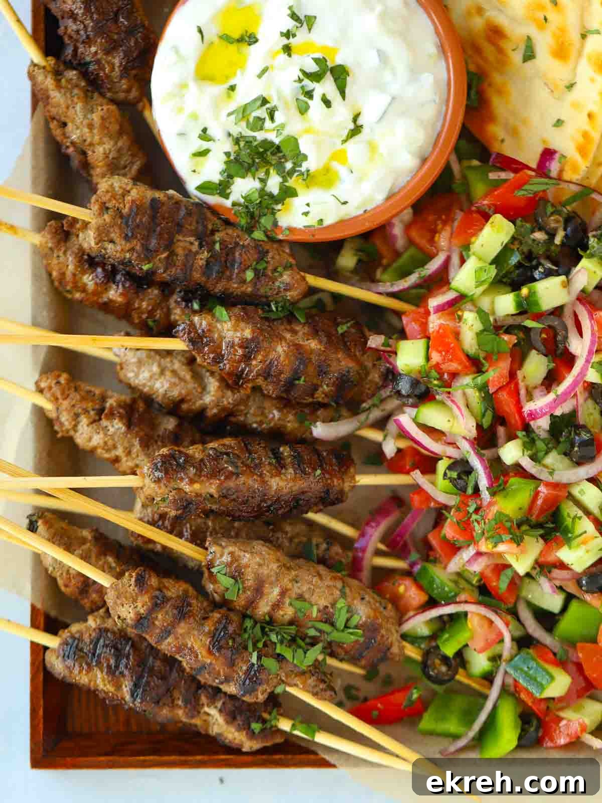 Spiced Lamb Koftas with Tzatziki Sauce 3 Lamb kofta kebabs recipe with flatbreads and Greek salad and tzatziki on a serving board, ready to eat.