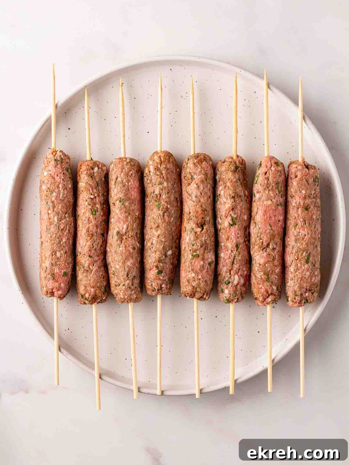 Spiced Lamb Koftas with Tzatziki Sauce 9 Raw lamb kofta kebabs with skewers through the middle, on a plate, ready to be cooked.