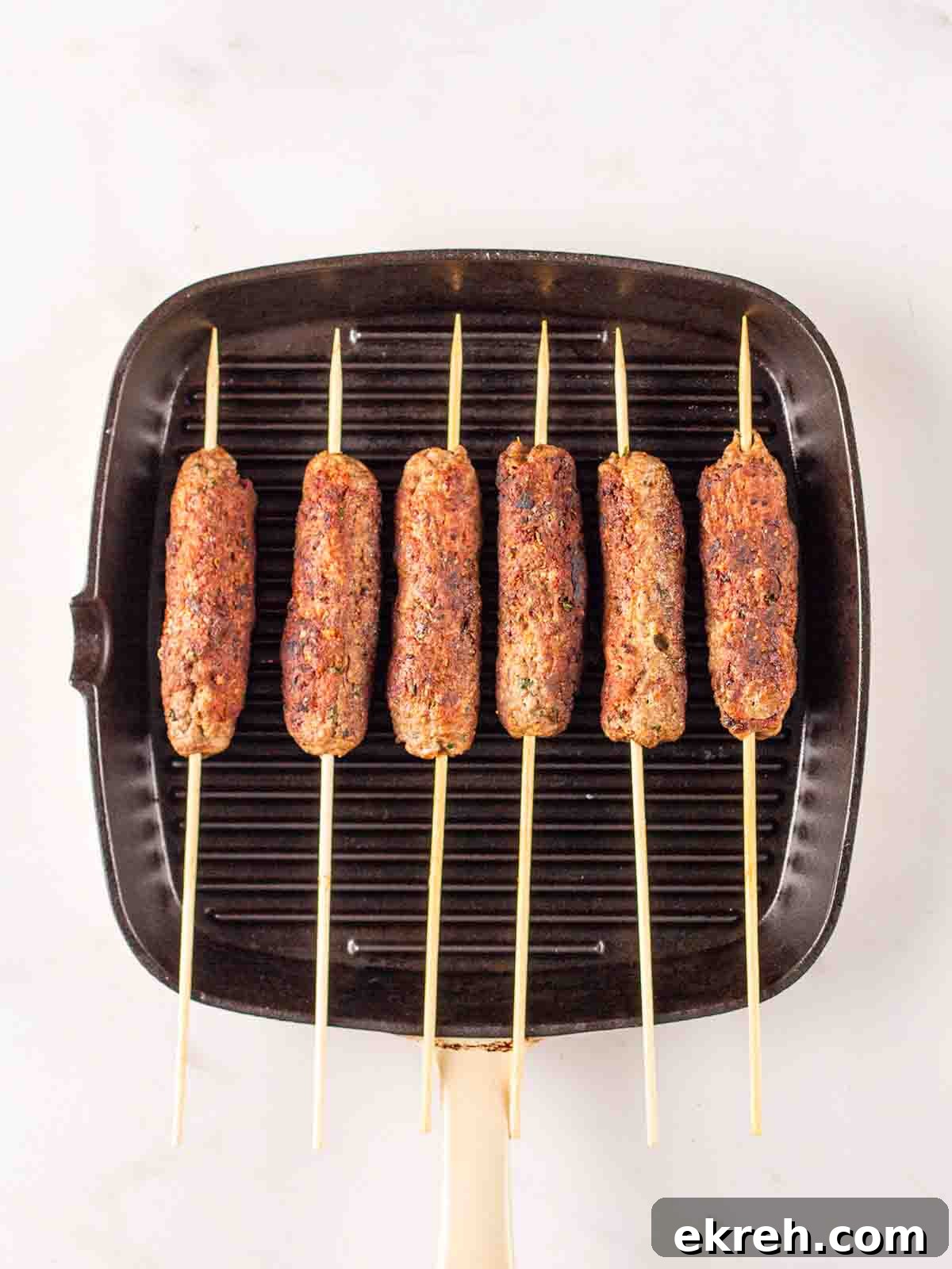Spiced Lamb Koftas with Tzatziki Sauce 10 Lamb mince koftas with skewers cooking on a griddle pan for step 3 in the recipe method.