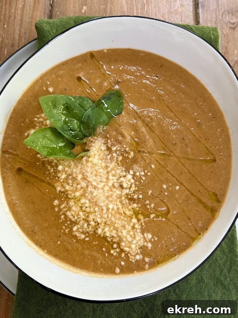 Creamy Eggplant Soup in white soup bowl with basil leaf, olive oil and grated cheese garnish, over green towel.