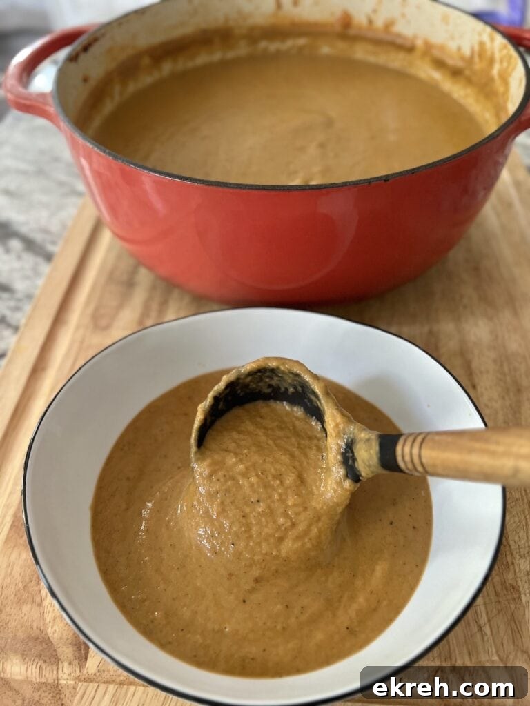 Using a ladle to pour creamy soup from Dutch oven into white soup bowl.