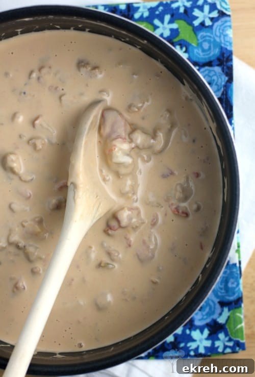 The finished sausage and Guiness extra stout beer cheese sauce in a saucepan with a wooden spoon; blue floral napkin in the background