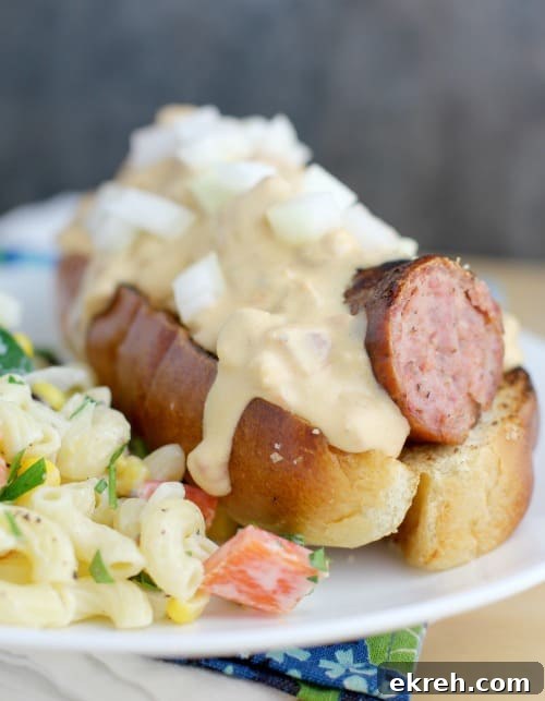 similar view of a finished beer kielbasa with queso, this time in a hot dog bun, white plate, with potato salad on the side