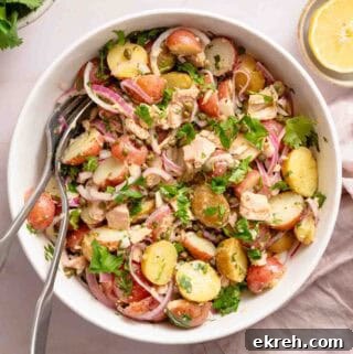 Classic Tuna and Potato Salad Recipe 10 potato and tuna salad in white bowl with serving spoons.