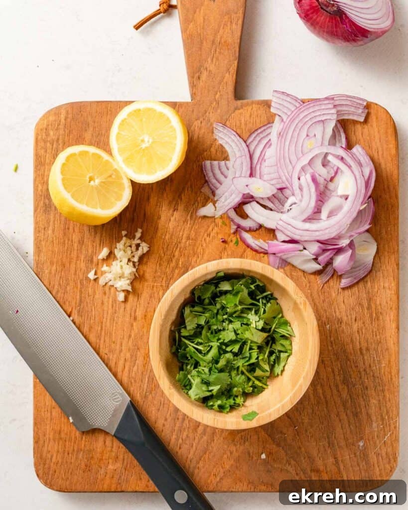 Classic Tuna and Potato Salad Recipe 5 cut cilantro in bowl on cutting board with lemon garlic and sliced onion on the side.