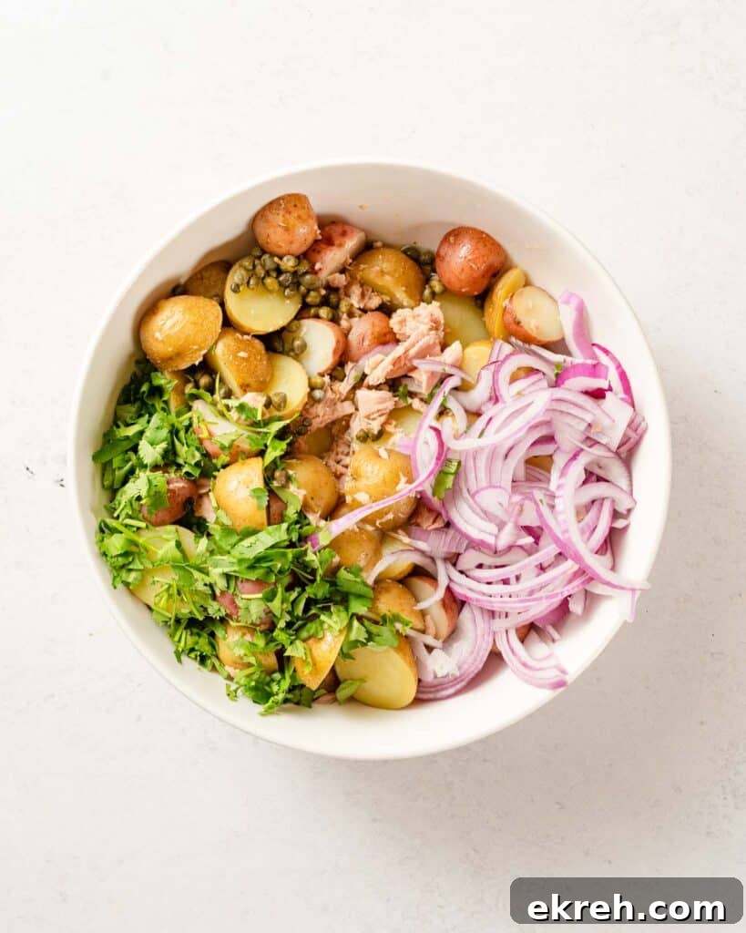 Classic Tuna and Potato Salad Recipe 7 potatoes herbs tuna and sliced onion in white bowl.