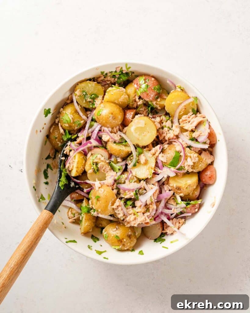 Classic Tuna and Potato Salad Recipe 8 tuna and potato salad mixed in white bowl with wooden spoon.