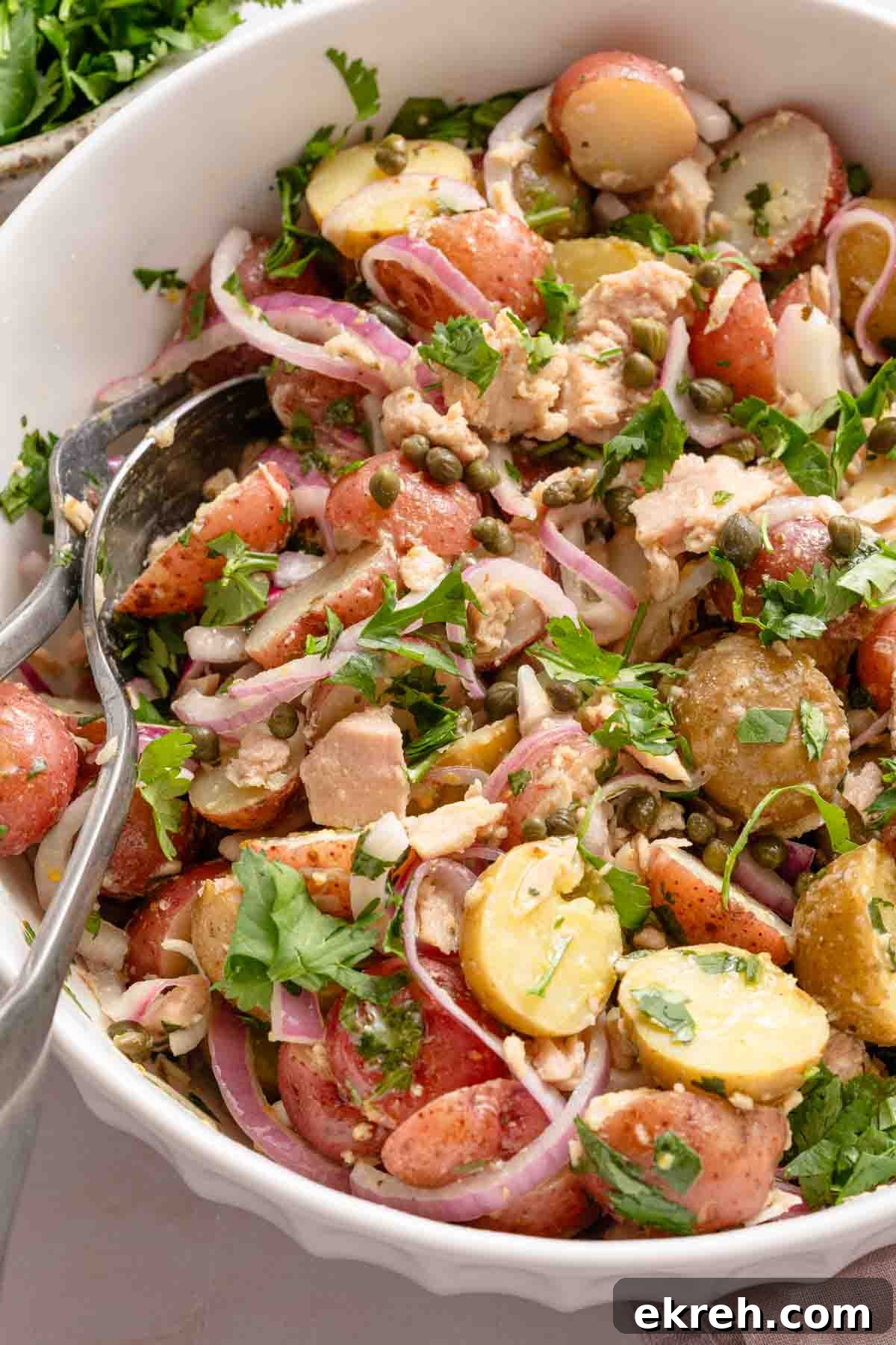 Classic Tuna and Potato Salad Recipe 9 spoon scooping up tuna and potato salad from white bowl.