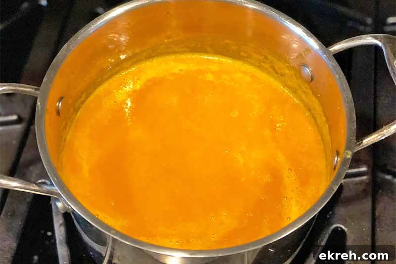 Dukkah-Spiced Roasted Carrot and Onion Soup Recipe 10 Horizontal image of a large pot filled with a bright orange pureed mixture on the stovetop.