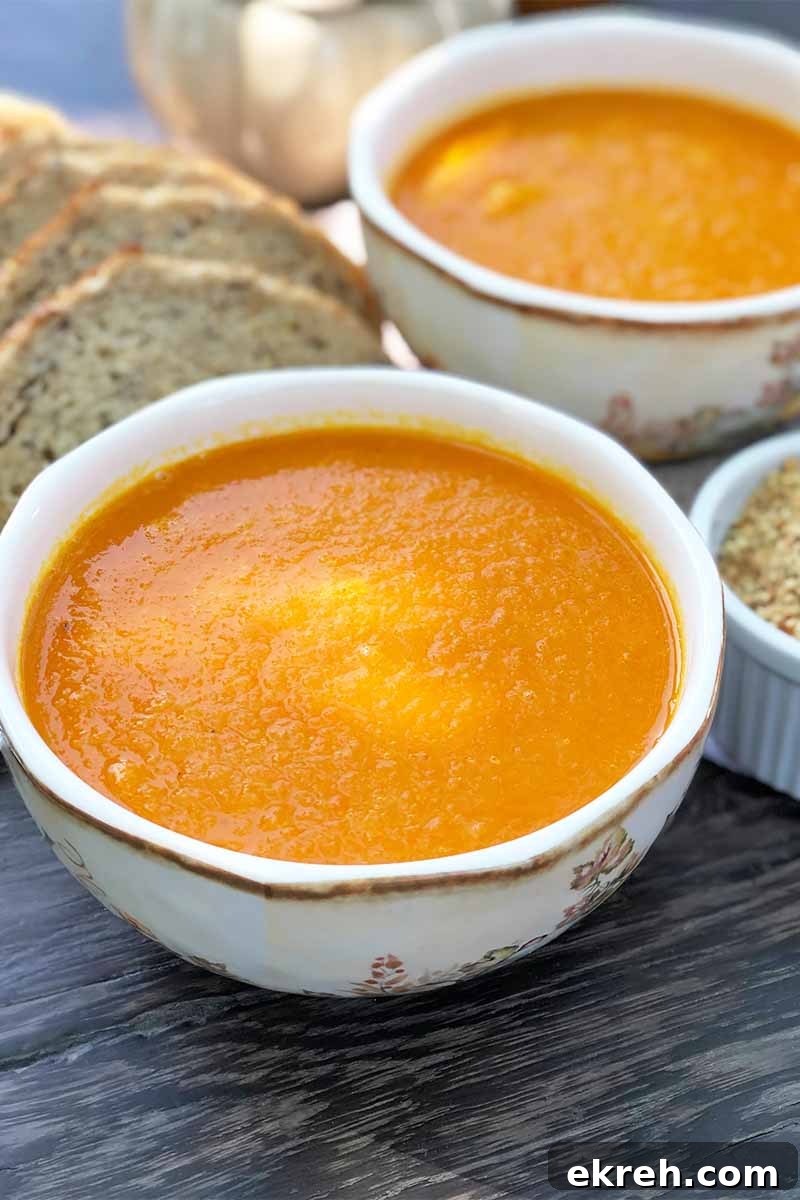 Dukkah-Spiced Roasted Carrot and Onion Soup Recipe 3 Vertical image of two white bowls filled with an orange puree next to slices of bread.