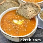 Horizontal image of a white bowl filled with an orange puree topped with yogurt and a nut garnish with a bread slice.