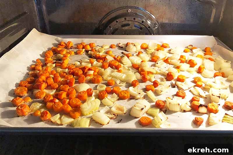 Dukkah-Spiced Roasted Carrot and Onion Soup Recipe 8 Horizontal image of roasting chopped carrots and onions on a lined baking sheet.