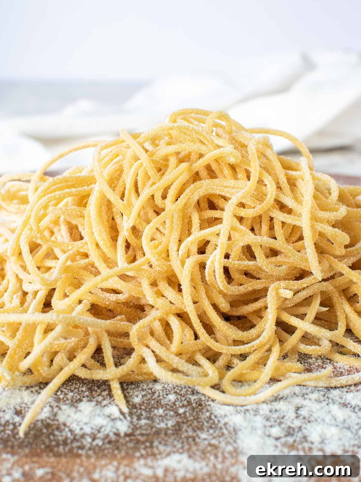 A pile of yellow homemade tonnarelli pasta on a wooden board.
