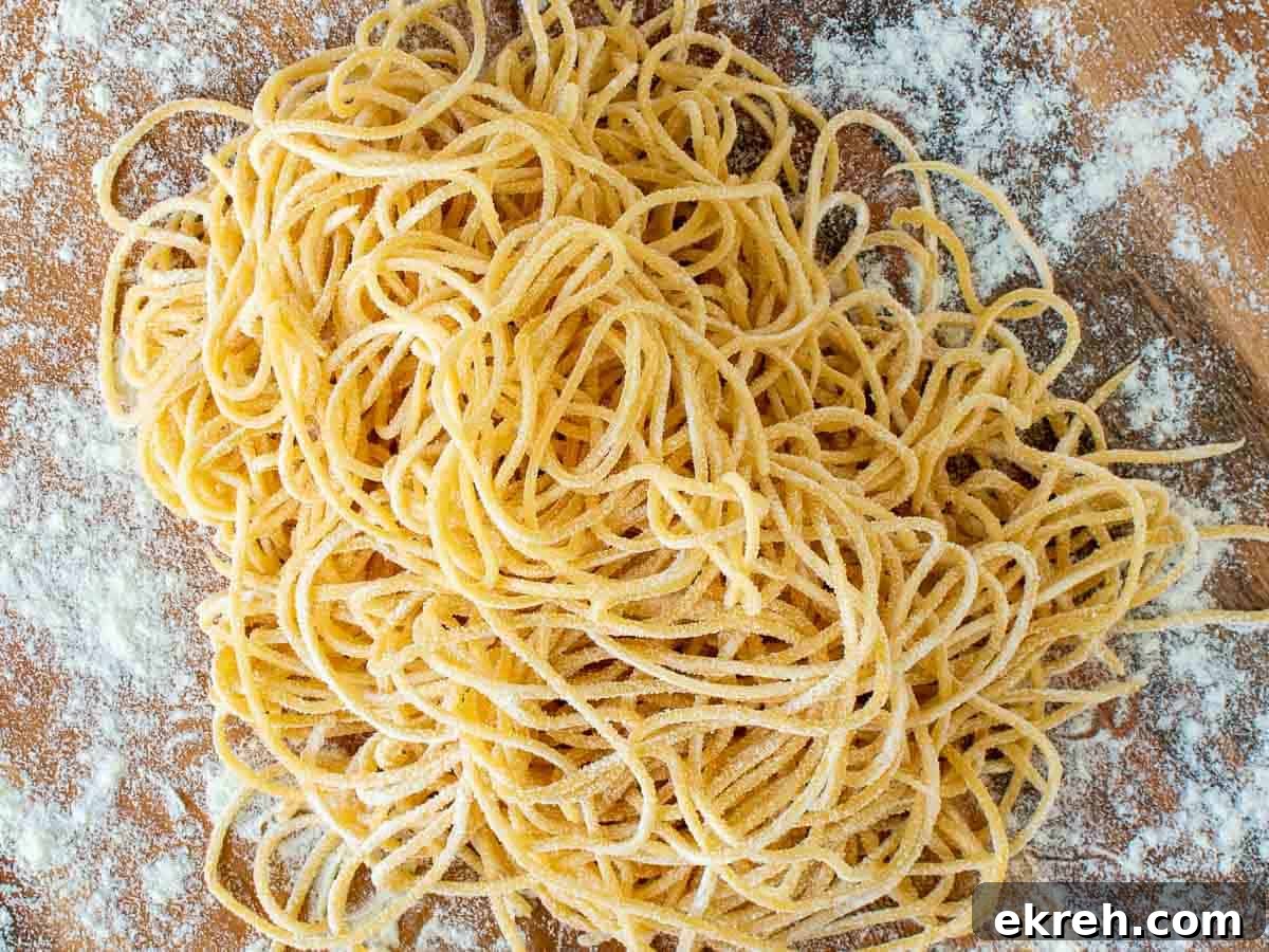 A pile of homemade tonnarelli pasta on a wooden board viewed from above.