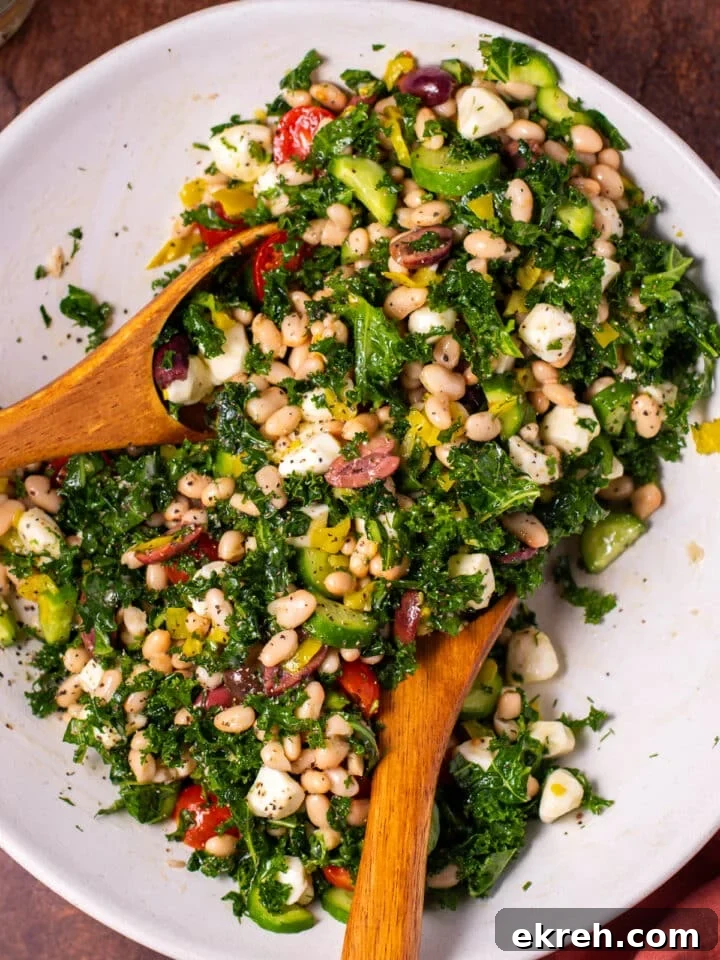 large white bowl with kale, white beans, tomatoes, cucumbers, mozzarella balls, olives, pepperoncinis and dressing