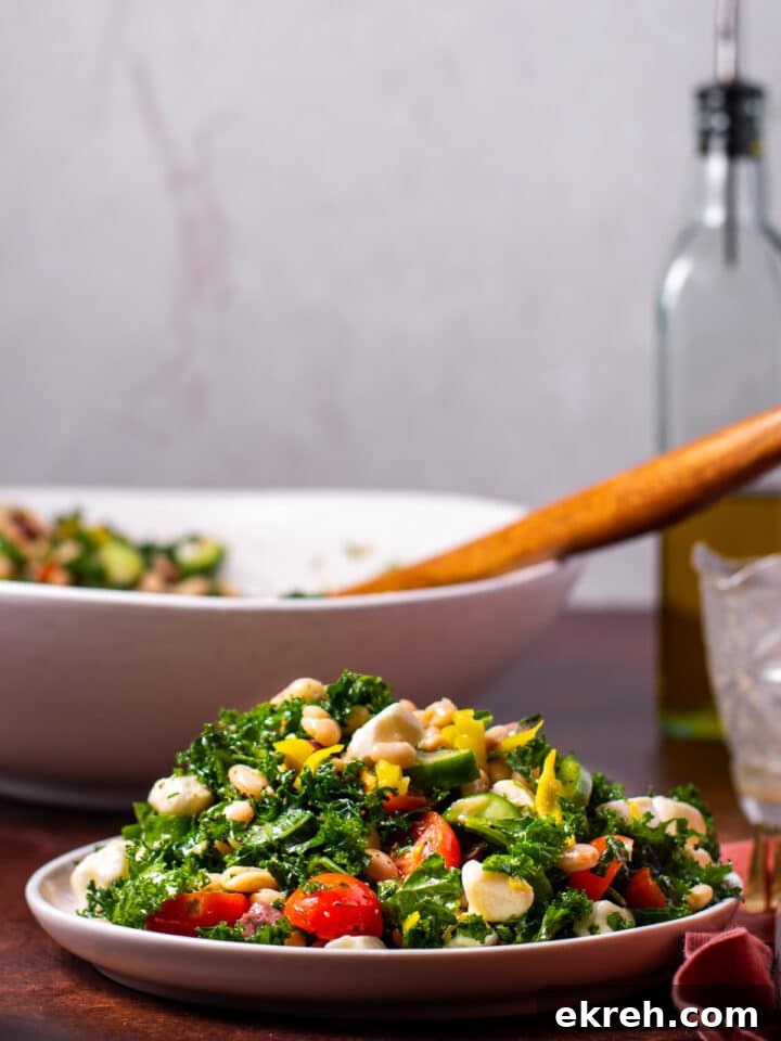 side angle of a pile of kale and white bean salad on a small plate, large salad bowl with wooden spoon in the background