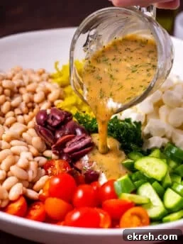 small glass pitcher of creamy herb dressing being poured over kale and cannellini bean salad