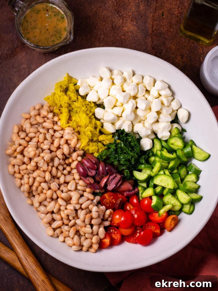 remaining salad ingredients added to the bowl: white beans, pepperoncinis, mozzarella pearls, olives, tomatoes and cucumbers