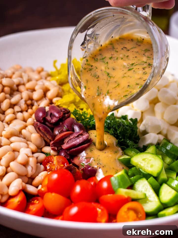 small crystal pitcher pouring dill mustard dressing on kale and cannellini bean salad