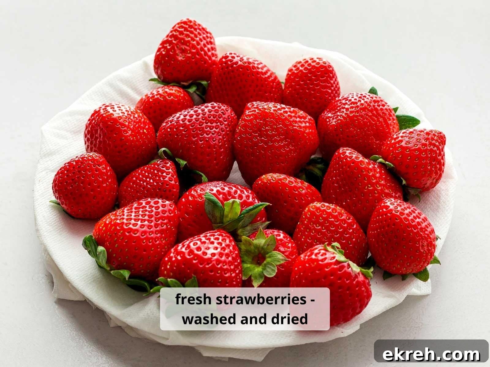 Red strawberries that are washed and dried on a white plate.