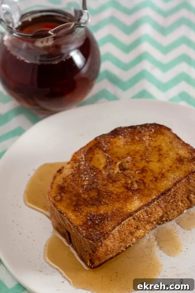Cinnamon Sugar Churro French Toast Recipe 2 An overhead view of two slices of churro French toast on a white plate in front of a pitcher of syrup