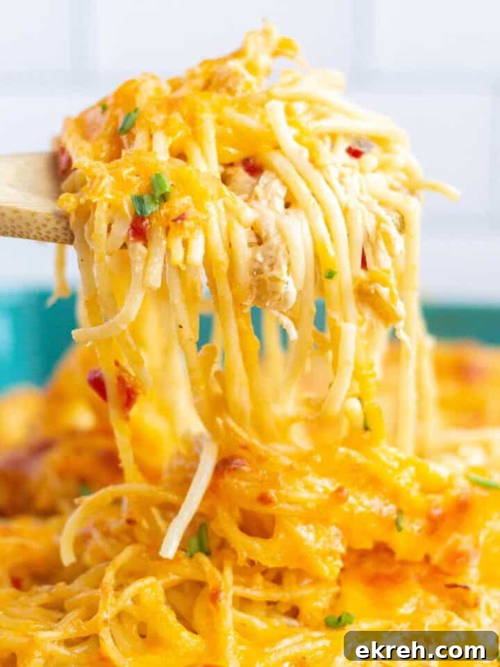 Rotel chicken spaghetti being scooped out of a baking dish by a wooden spoon.