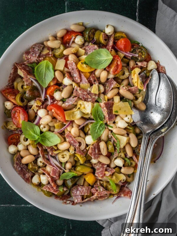 Bean antipasto salad with salami, cherry tomatoes, fresh basil garnish in a bow.