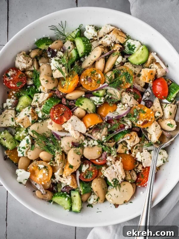 Greek chicken salad with butter beans, cherry tomatoes, feta and cucumbers garnished with fresh dill fronds in a large serving bowl.