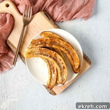 Air fryer bananas on a white plate over a rustic wooden cutting board with a pink linen and a copper fork.