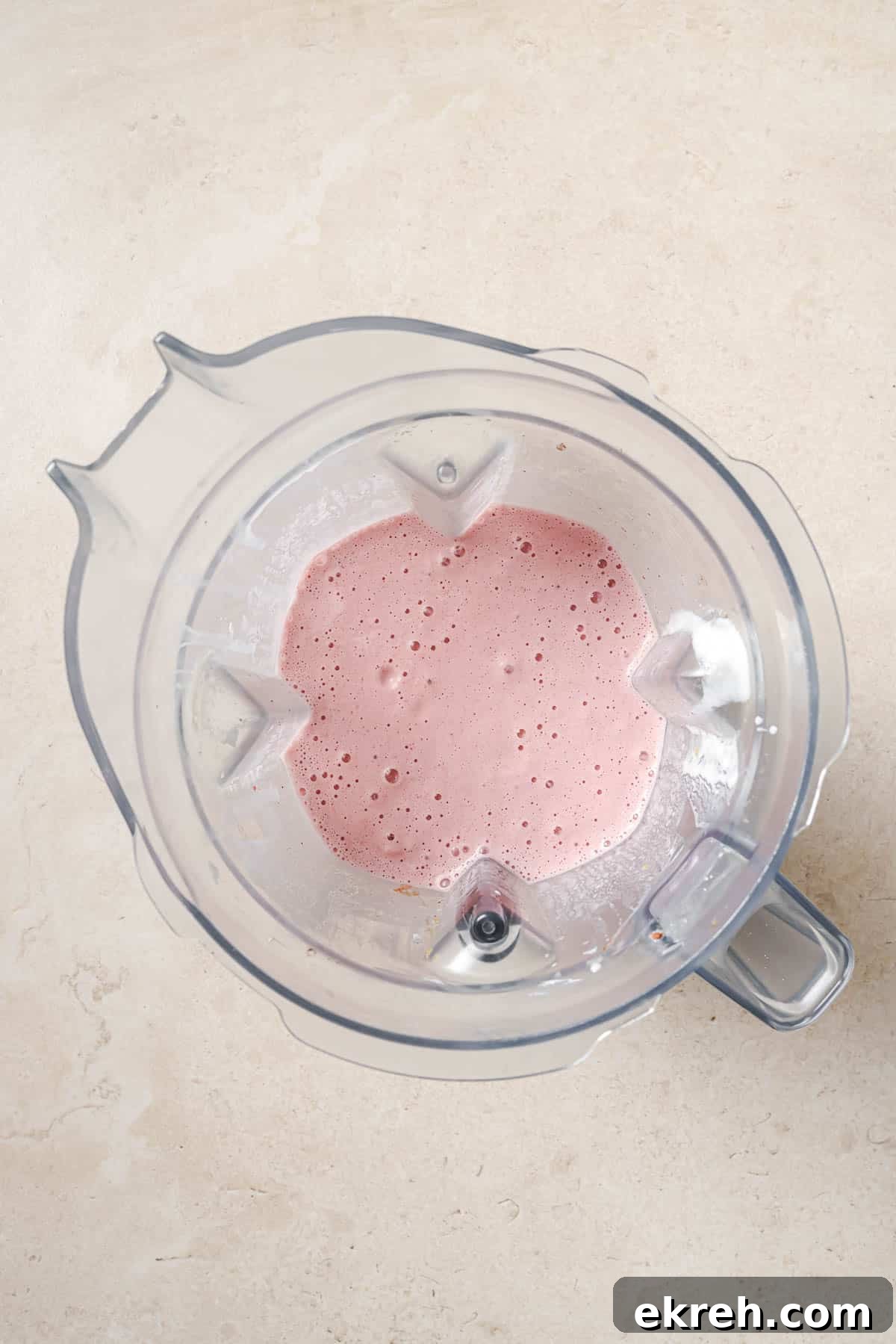 Top view of a blender containing a pink, frothy liquid blend on a light beige counter.