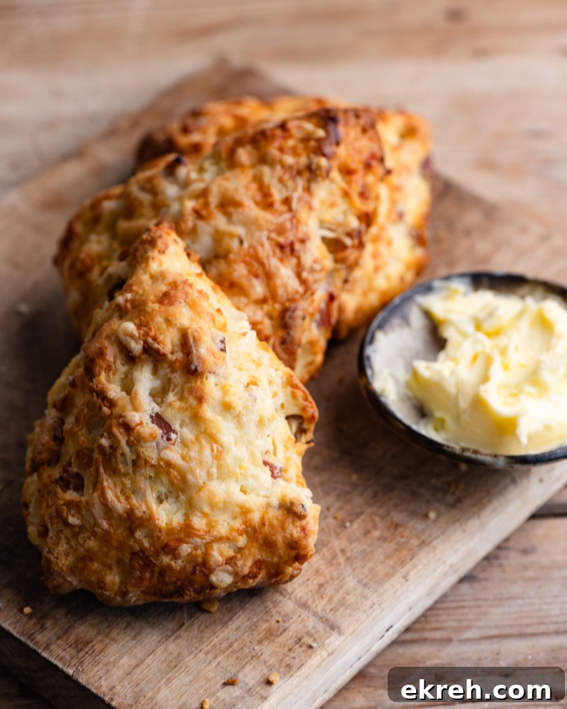 Three triangle shaped bacon and cheese scones on a wooden cutting board next to a small bowl of whipped butter.