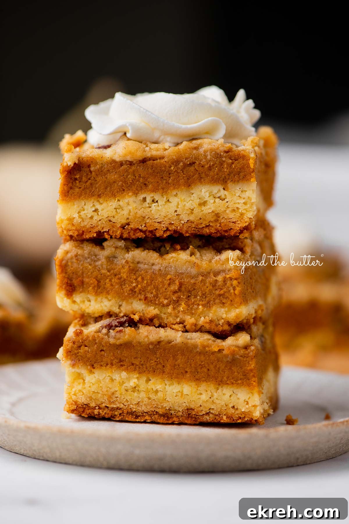 Pumpkin Pie Cake Bars Recipe 2 Stack of three pumpkin pie cake bars on a parchment paper lined bottom | © Beyond the Butter®