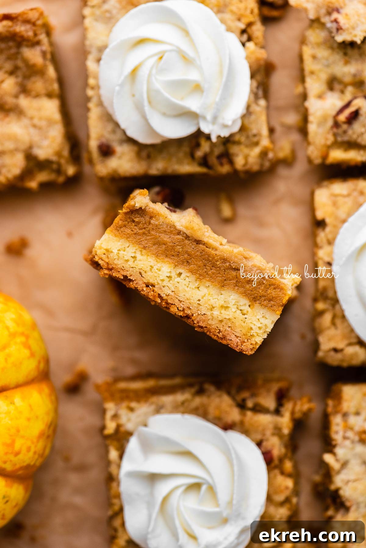 Pumpkin Pie Cake Bars Recipe 3 Sliced pumpkin pie cake bars on parchment paper background with center slice on its side | © Beyond the Butter®