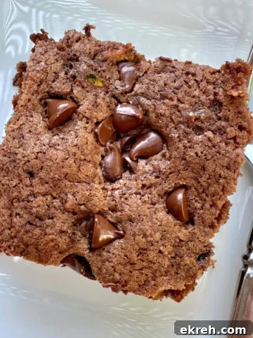 A serving of moist chocolate zucchini cake on a plate with a fork.