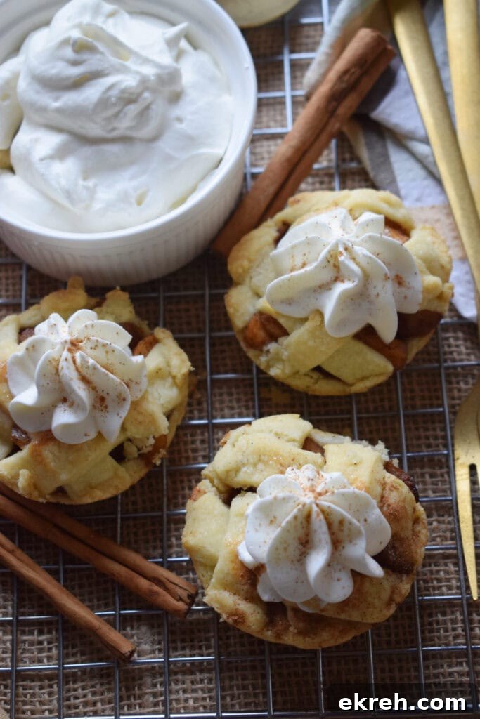Whipped cream topped mini apple pies with a bowl of whipped cream.