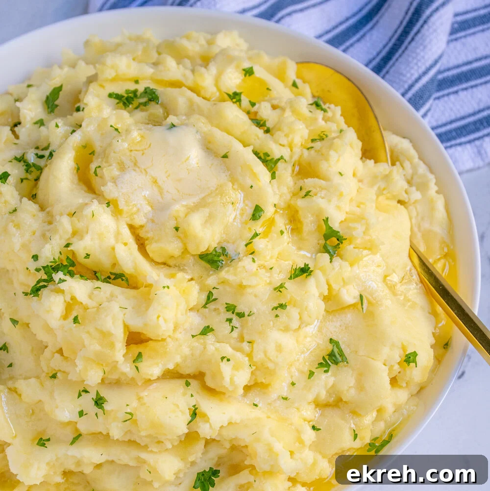 White bowl full of fluffy mashed potatoes dripping with melted butter and garnished with fresh parsley.