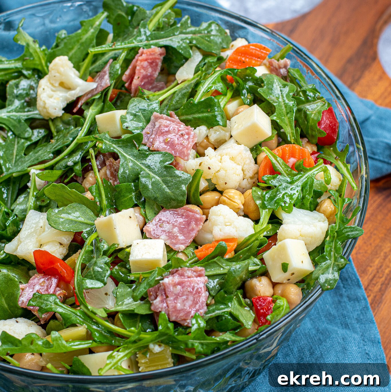 A tossed easy antipasto salad in a glass salad bowl showing off cheese cubes, salami, and pickled vegetables.