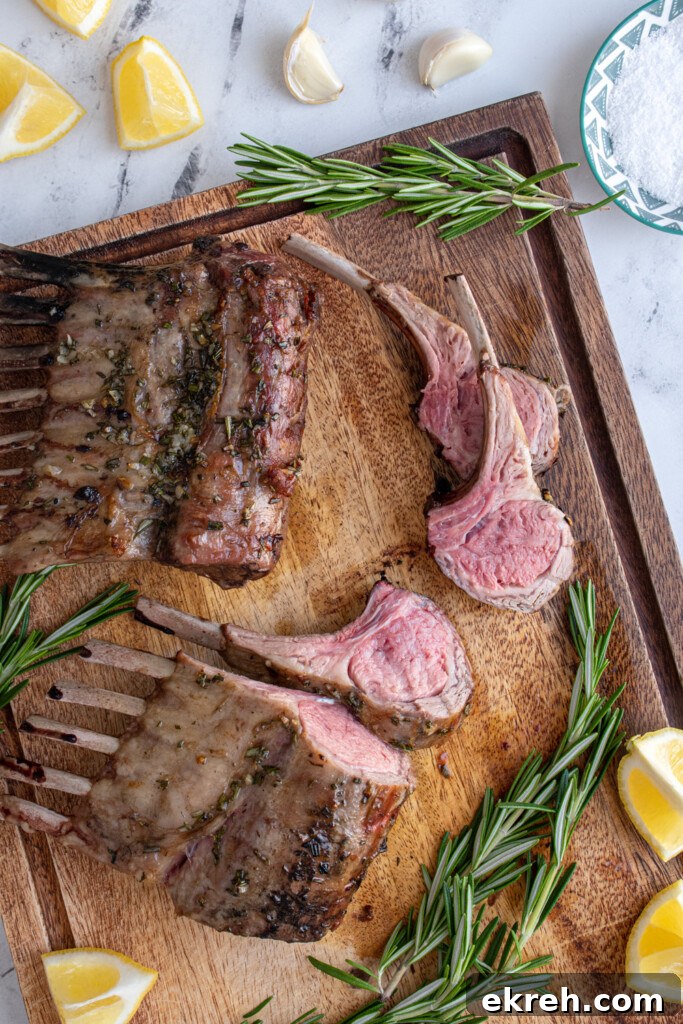 Wooden cutting board with two rack of grilled lamb with the first three pieces cut off showing a pink lamb interior.