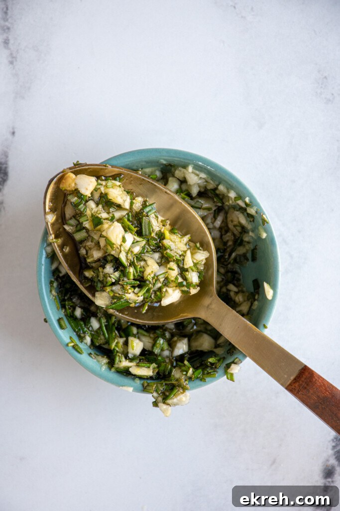 A small bowl with a spoon full of the olive oil, garlic, rosemary mixture for the grilled lamb.