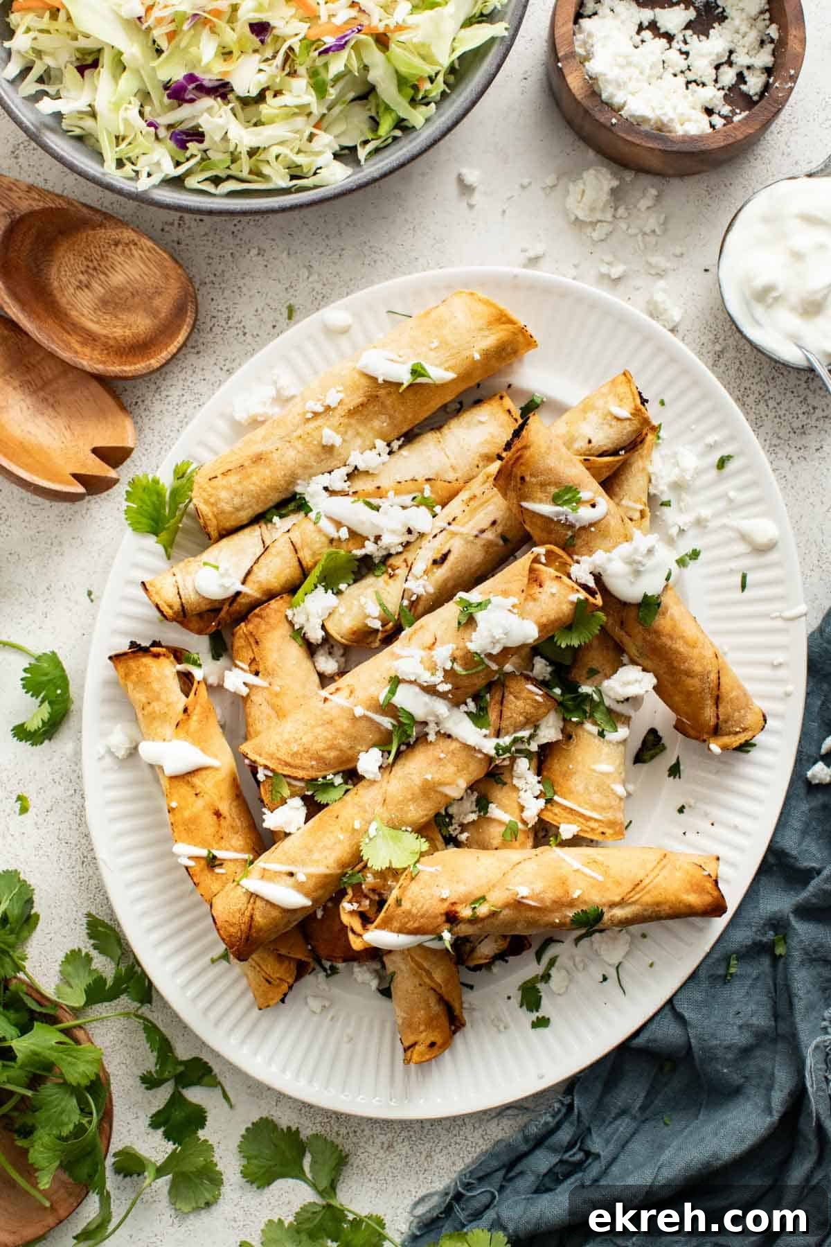 How to Make Crispy Air Fryer Chicken Taquitos 2 Chicken taquitos stacked on a white plate, drizzled with sour cream sauce and cilantro.