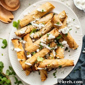 How to Make Crispy Air Fryer Chicken Taquitos 11 Crispy chicken taquitos on a white plate with sour cream dipping sauce, cilantro, and crumbled cheese.