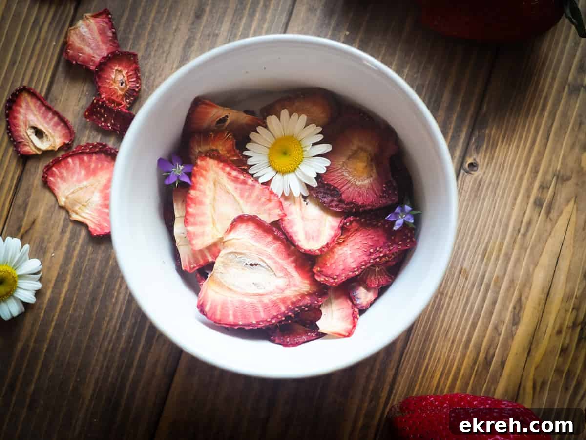 A bowl of dehydrated strawberries on a wood background with some daisies and small purple flowers scattered around.