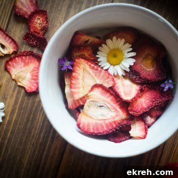 A bowl of dehydrated strawberries on a wood background with some daisies and small purple flowers scattered around.