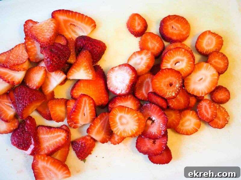 Sliced strawberries on a white cutting board.