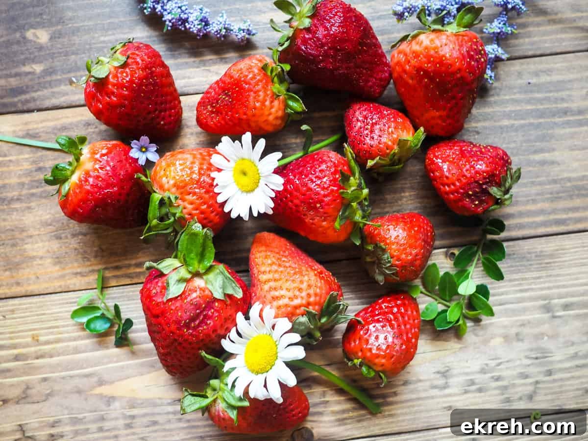 A bunch of overripe strawberries laid out on a wooden surface with daisies and purple flowers scattered around.