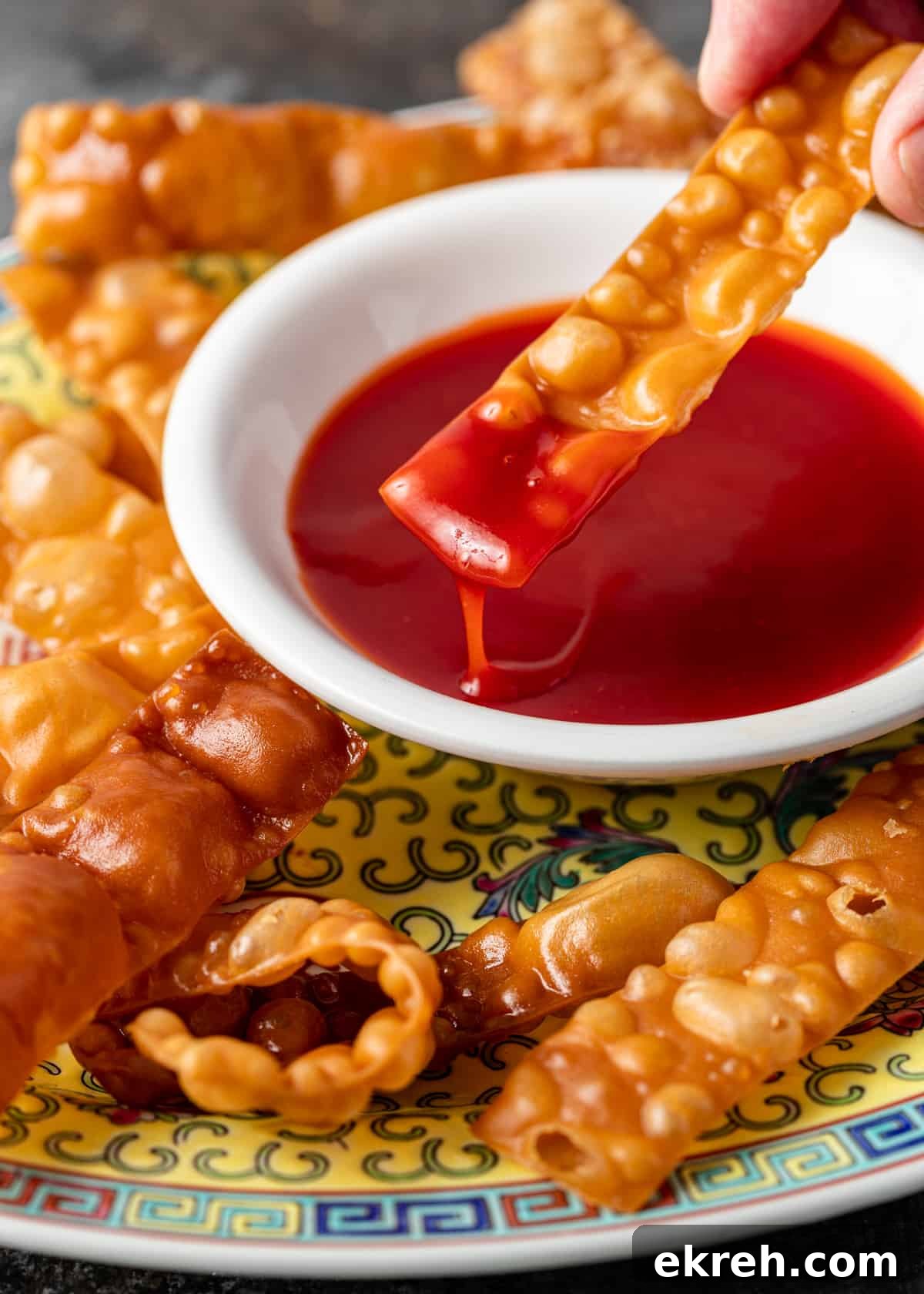 Homemade Sweet and Sour Sauce Recipe for Stir-Fries and Dipping 7 closeup side view: sweet and sour sauce in white bowl on top of colorful platter with wonton strips