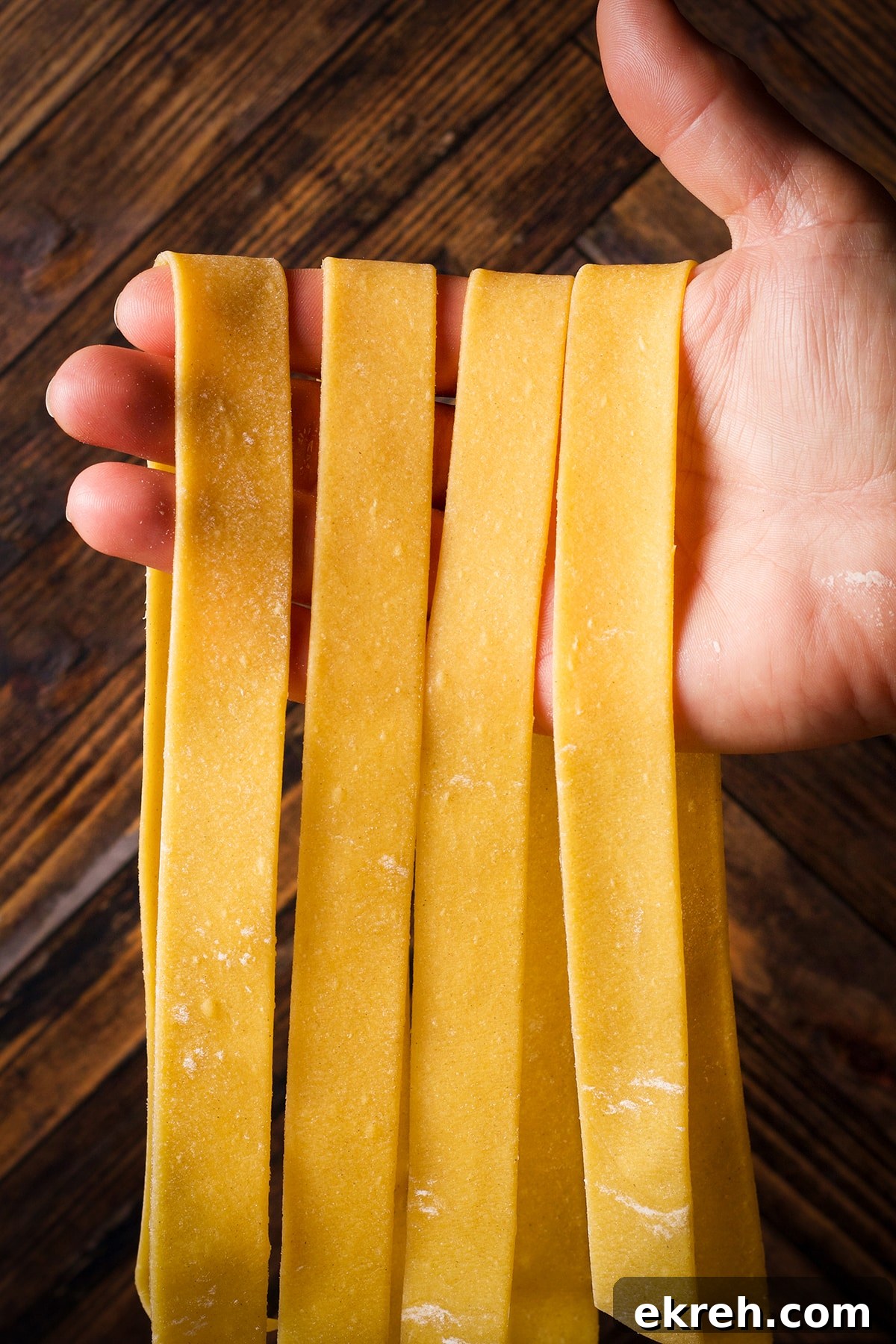 Holding up several homemade pappardelle noodles .
