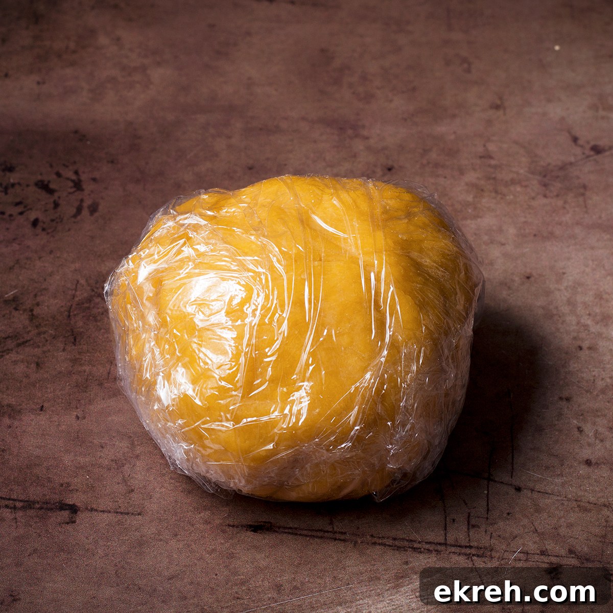 A ball of homemade pasta dough that's been wrapped in plastic wrap.